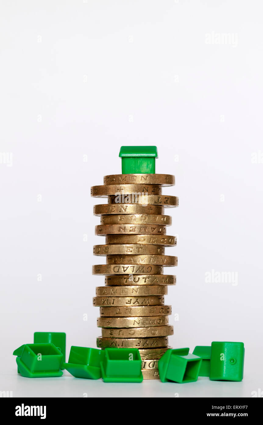 Un piccolo modello di plastica casa verde sulla cima di un palo di libbra di monete nel mezzo di case capovolta. Finanziamento di alloggi concetto. Foto Stock