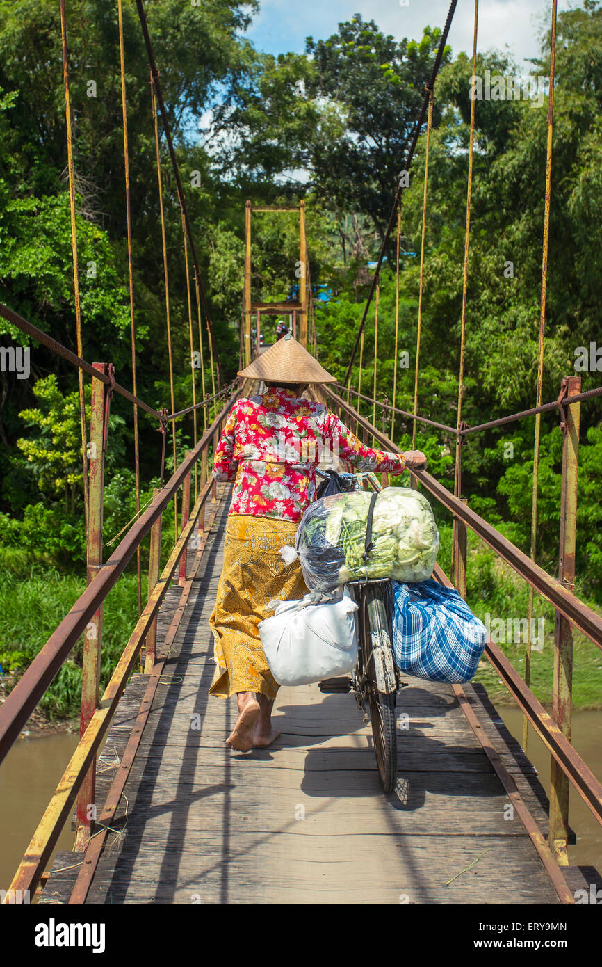 Donna indonesiana nel tradizionale hat borse e zaini sulla sua bicicletta attraverso il ponte Foto Stock