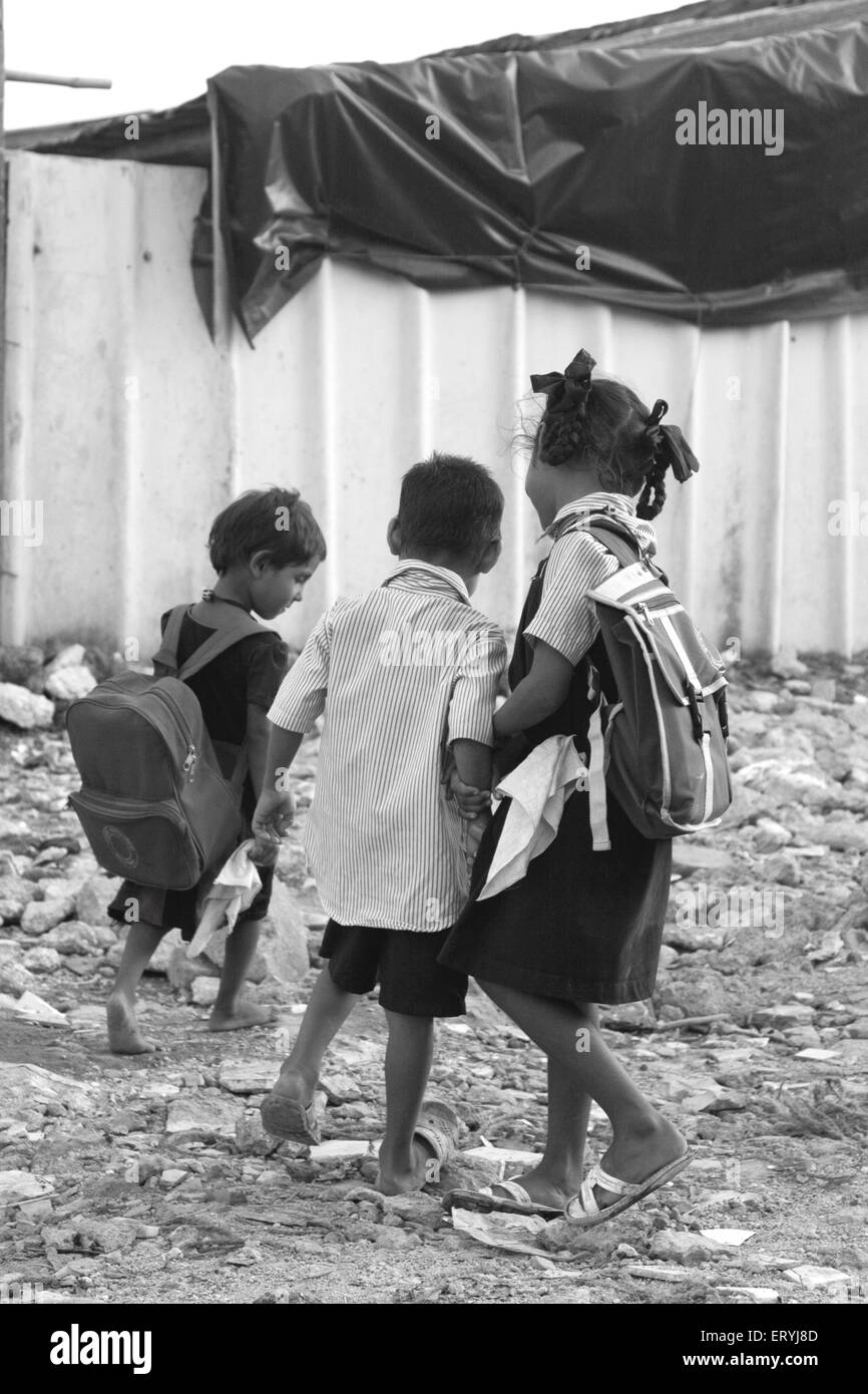 Scolaresche che trasportano borse pesanti Malvani slum Malad Bombay Mumbai Maharashtra India scuola indiana che va ragazze Foto Stock