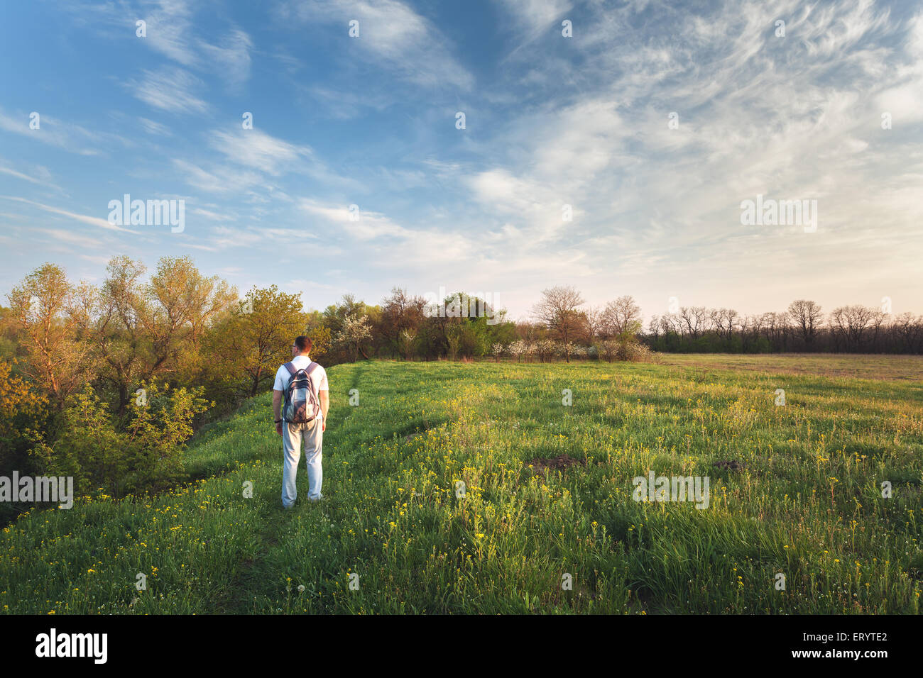 Bel tramonto. La molla del paesaggio con uomo sul campo. Alberi, cielo blu e nuvole Foto Stock