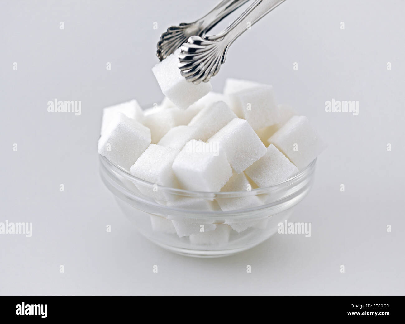 Zollette di zucchero in un recipiente di vetro con le pinze Foto Stock