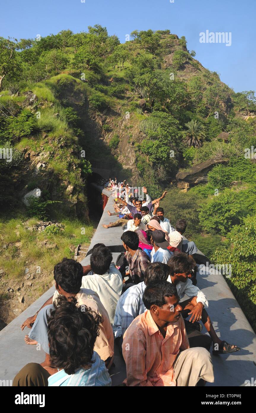 Le persone che assumono il rischio durante il viaggio sul tetto del treno diretto attraverso il tunnel ; Rajasthan ; India Foto Stock