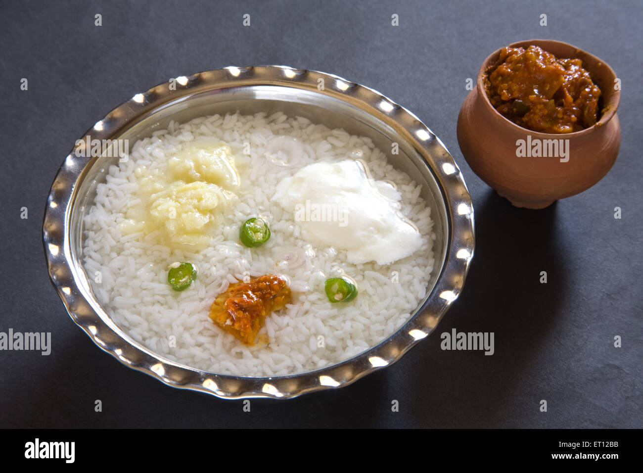 Pranzo indiano pakhala riso pickle schiacciare le patate con peperoncino e yogurt in acciaio ciotola con sottaceti in pentola di terra su sfondo nero Foto Stock