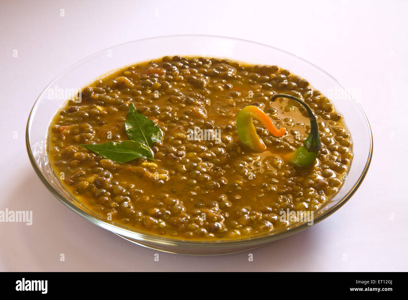 Indian masoor dal red grammo zuppa di lenticchie guarnite con foglie di curry e peperoncino in vaso di vetro su sfondo bianco Foto Stock