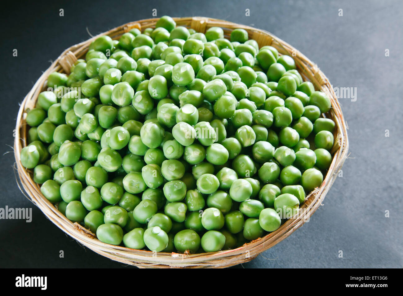Piselli verdi in cestino di canna su sfondo nero Foto Stock
