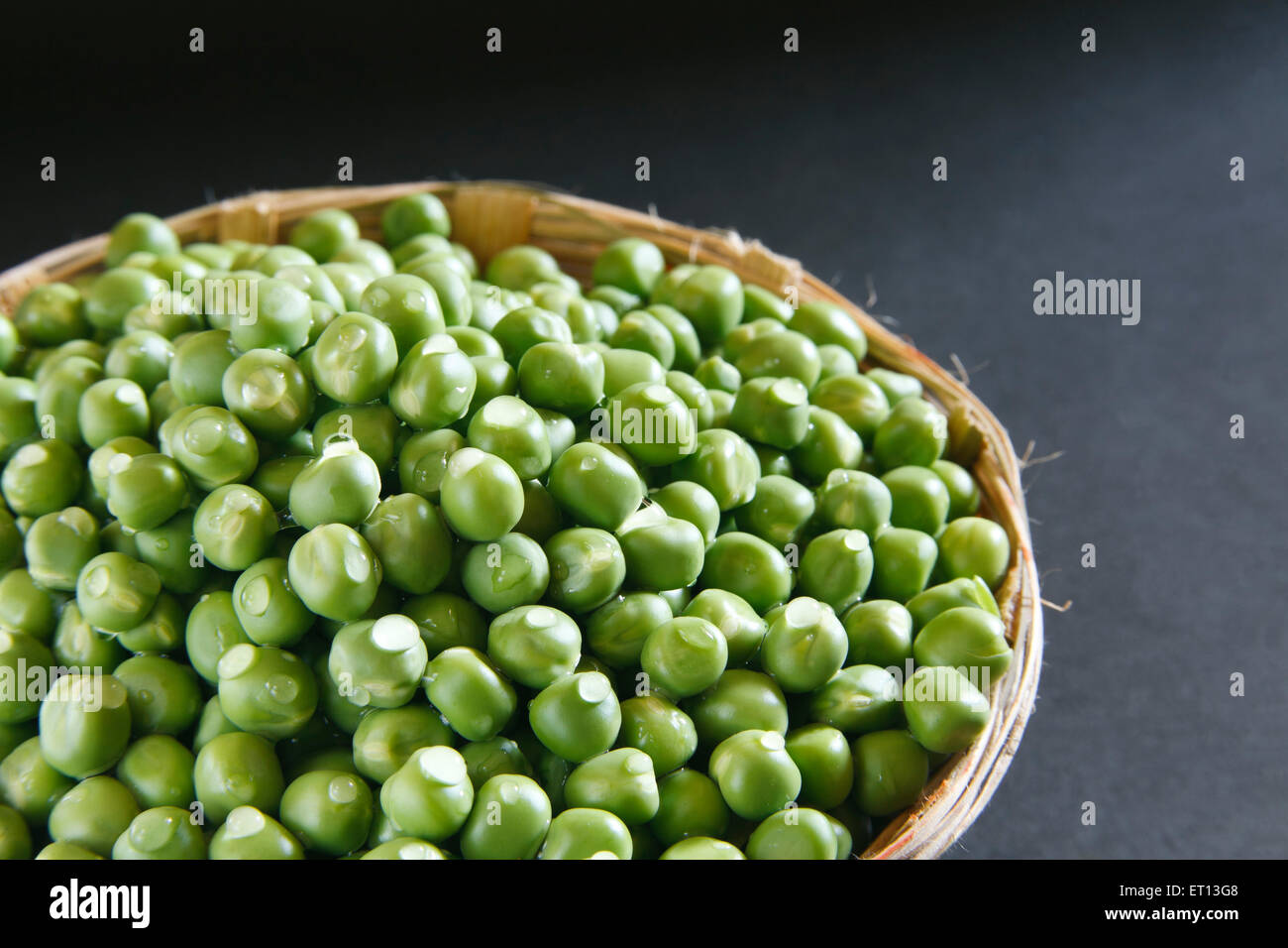 Piselli verdi in cestino di canna su sfondo nero Foto Stock