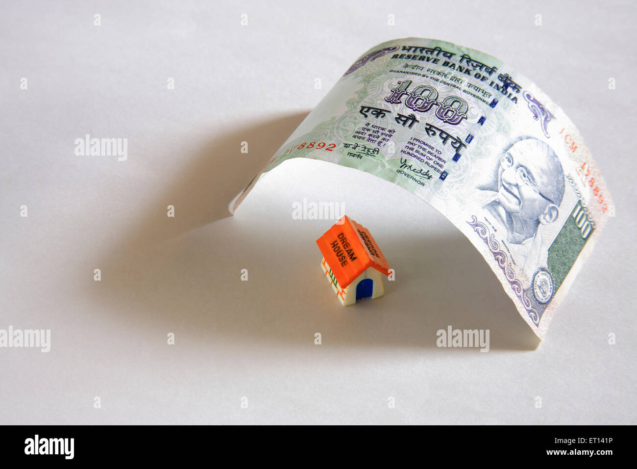 Prestito di alloggiamento, modello domestico di plastica sotto cento nota di rupie su sfondo bianco Foto Stock