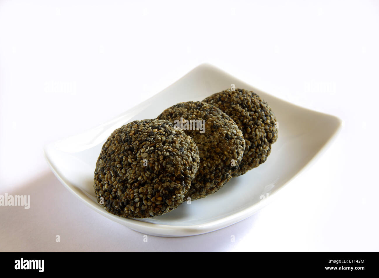 Dolce indiano , Ladoo Tilgur, Ladoo tilgul, Ladoo di semi di sesamo nero, in piastra su sfondo bianco Foto Stock