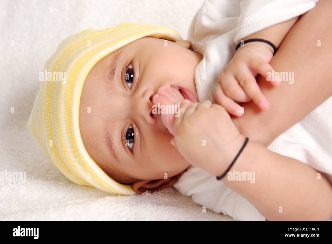Il bambino succhia toe indossando il cappuccio e amuleti intorno a mani signor#736LA Foto Stock
