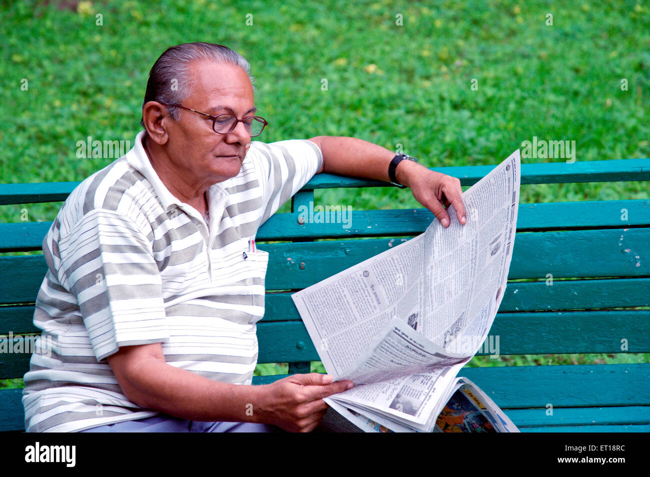 Indian senior citizen leggendo il giornale seduto giardino verde banco - signor#364 Foto Stock