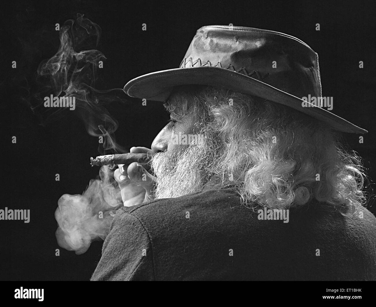 vecchio che indossa un cappello che fuma sigaro barba bianca sfondo nero e bianco nero scatto studio Foto Stock