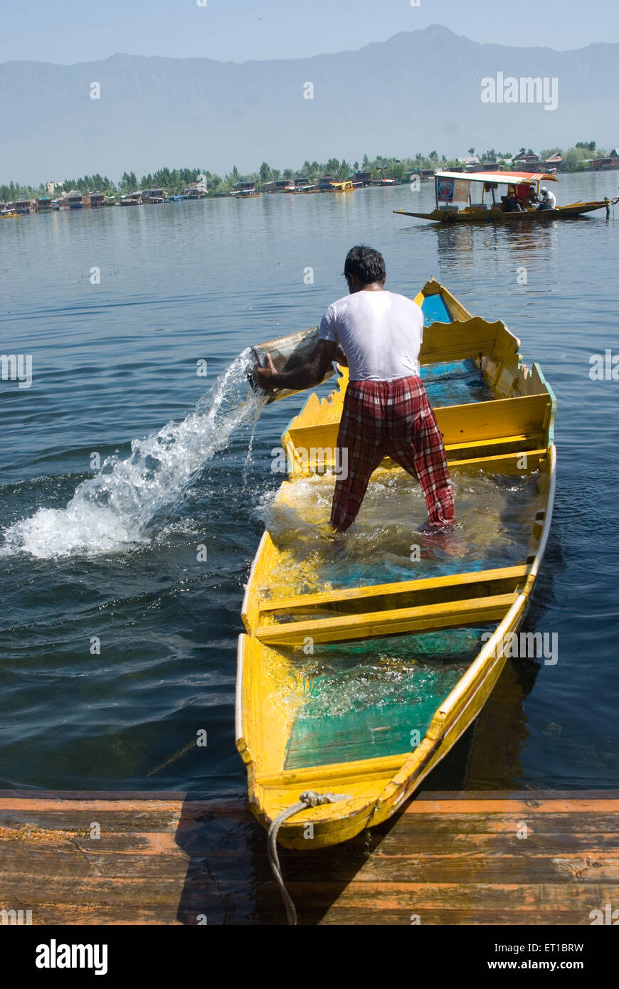 Uomo che lancia acqua dalla sua barca nel lago dal; Srinagar; Jammu e Kashmir; India; Asia Foto Stock