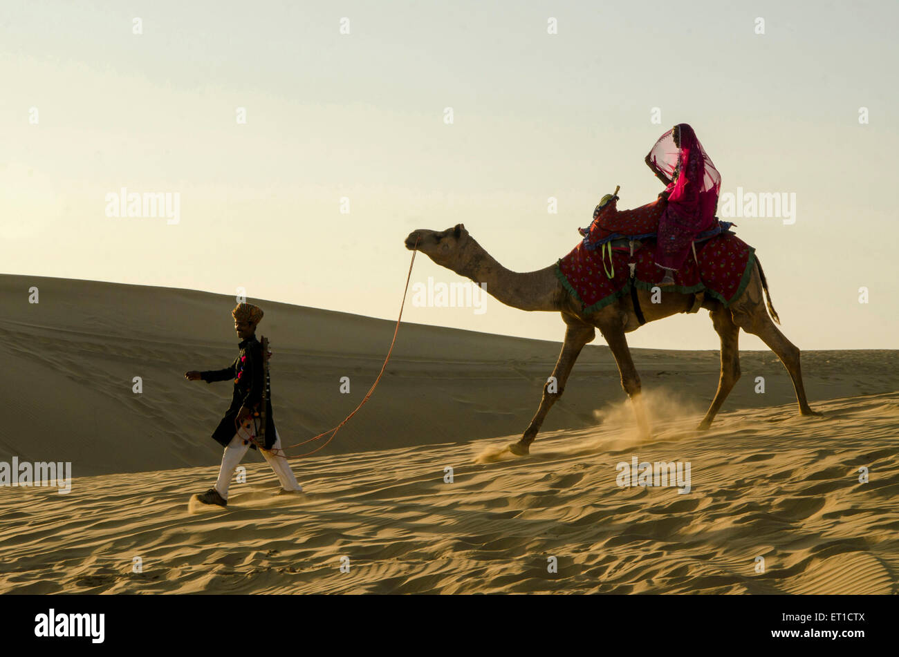 L'uomo trascinando cammello con donna seduta su di esso duna di sabbia Jaisalmer Rajasthan India Asia MR # 704 Foto Stock
