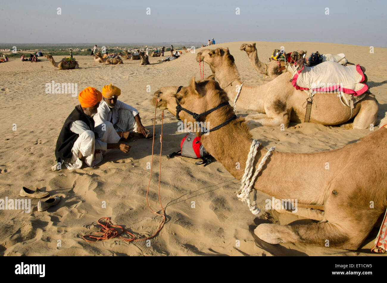 Uomini e cammello seduto sulla duna di sabbia in attesa di safari turistici in Khuri a Jaisalmer Rajasthan India Asia Foto Stock