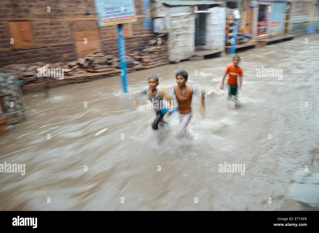 Ragazzi in esecuzione alluvione di fuga di acqua sulla strada Mohalla Makrana monsone di Jodhpur Rajasthan in India Foto Stock
