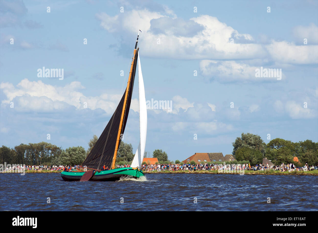 Uno storico fondo piatto in barca a vela è su uno dei laghi della Frisia con gli spettatori a guardare skûtsjesilen in Olanda Foto Stock