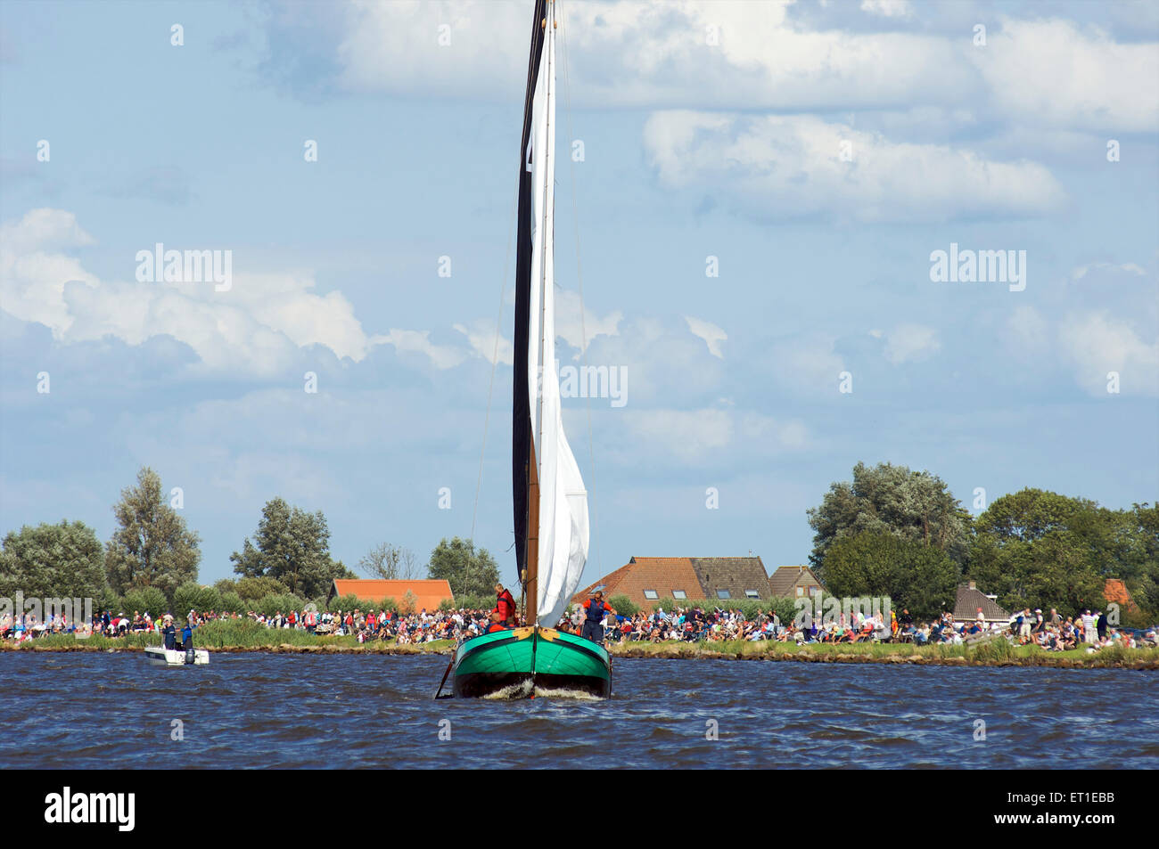 Uno storico fondo piatto in barca a vela è su uno dei laghi della Frisia con gli spettatori a guardare skûtsjesilen in Olanda Foto Stock