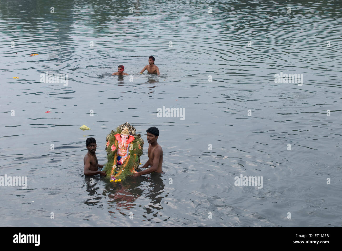 Un piccolo idolo del Signore Ganesh prese da due menfor immersione in acqua Pune India Asia Foto Stock