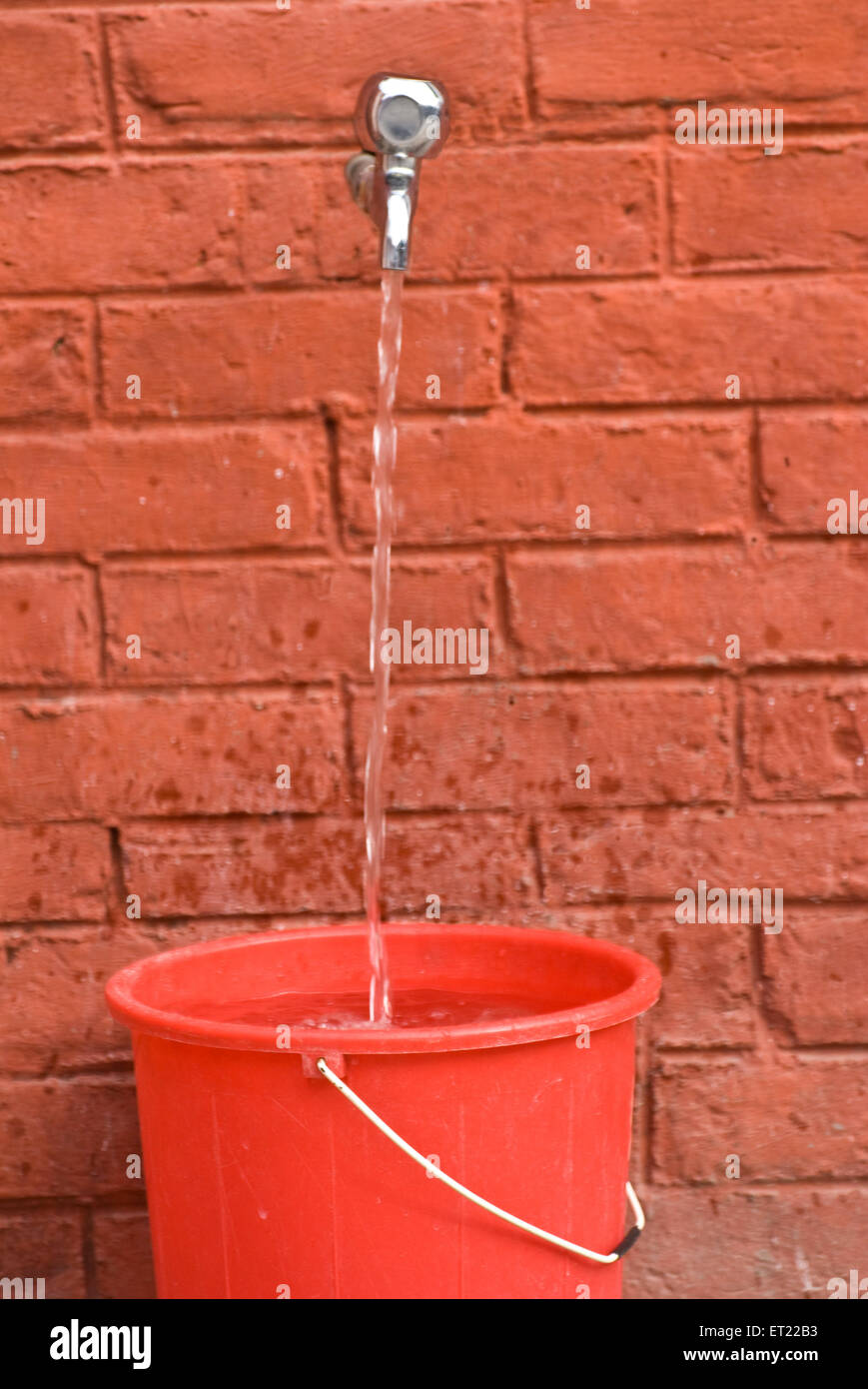 Acqua di rubinetto che riempie il secchio rosso di plastica, India, Asia Foto Stock
