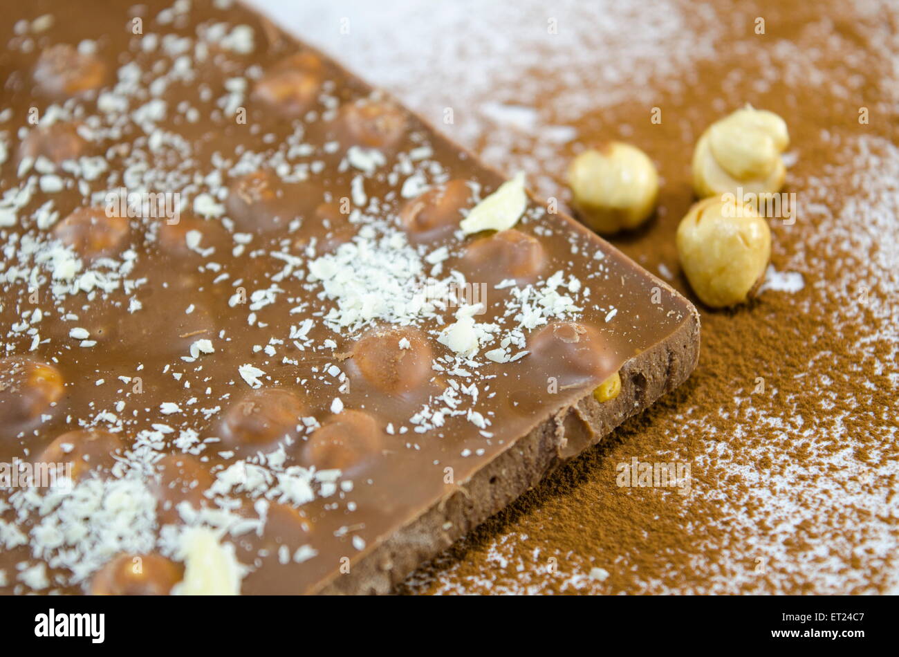 Il cioccolato con le nocciole su una superficie cosparsa di cacao e polvere di noce di cocco Foto Stock