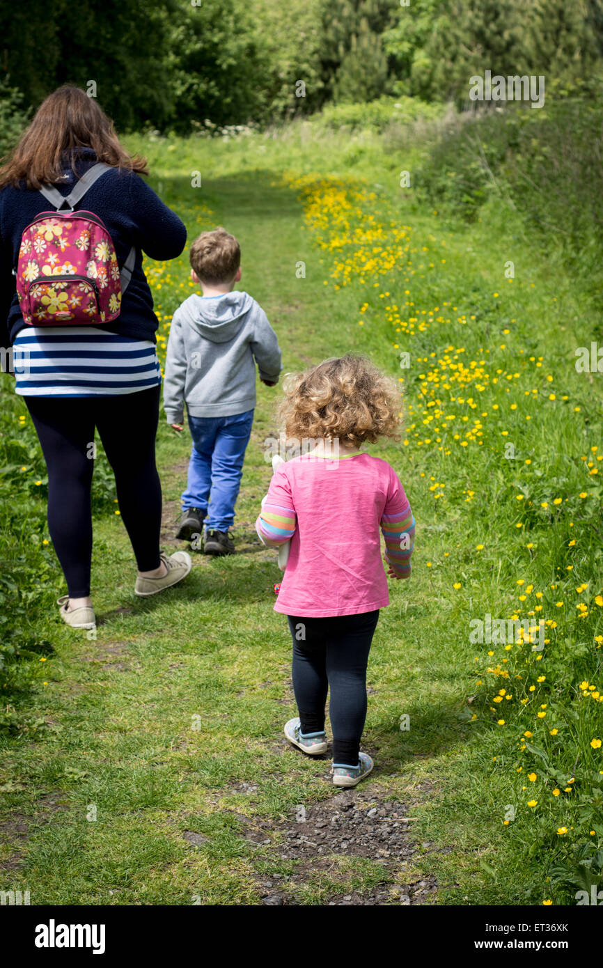 Madre e bambini ragazza ragazzo famiglia seguente una cartina passeggiate in campagna con il sole splendente e nuvole nel cielo Foto Stock