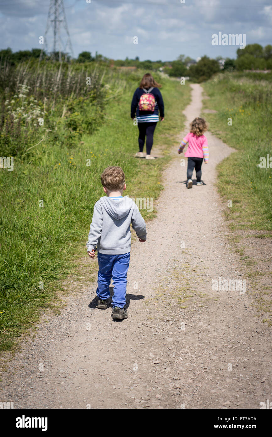 Madre e bambini ragazza ragazzo famiglia seguente una cartina passeggiate in campagna con il sole splendente e nuvole nel cielo Foto Stock