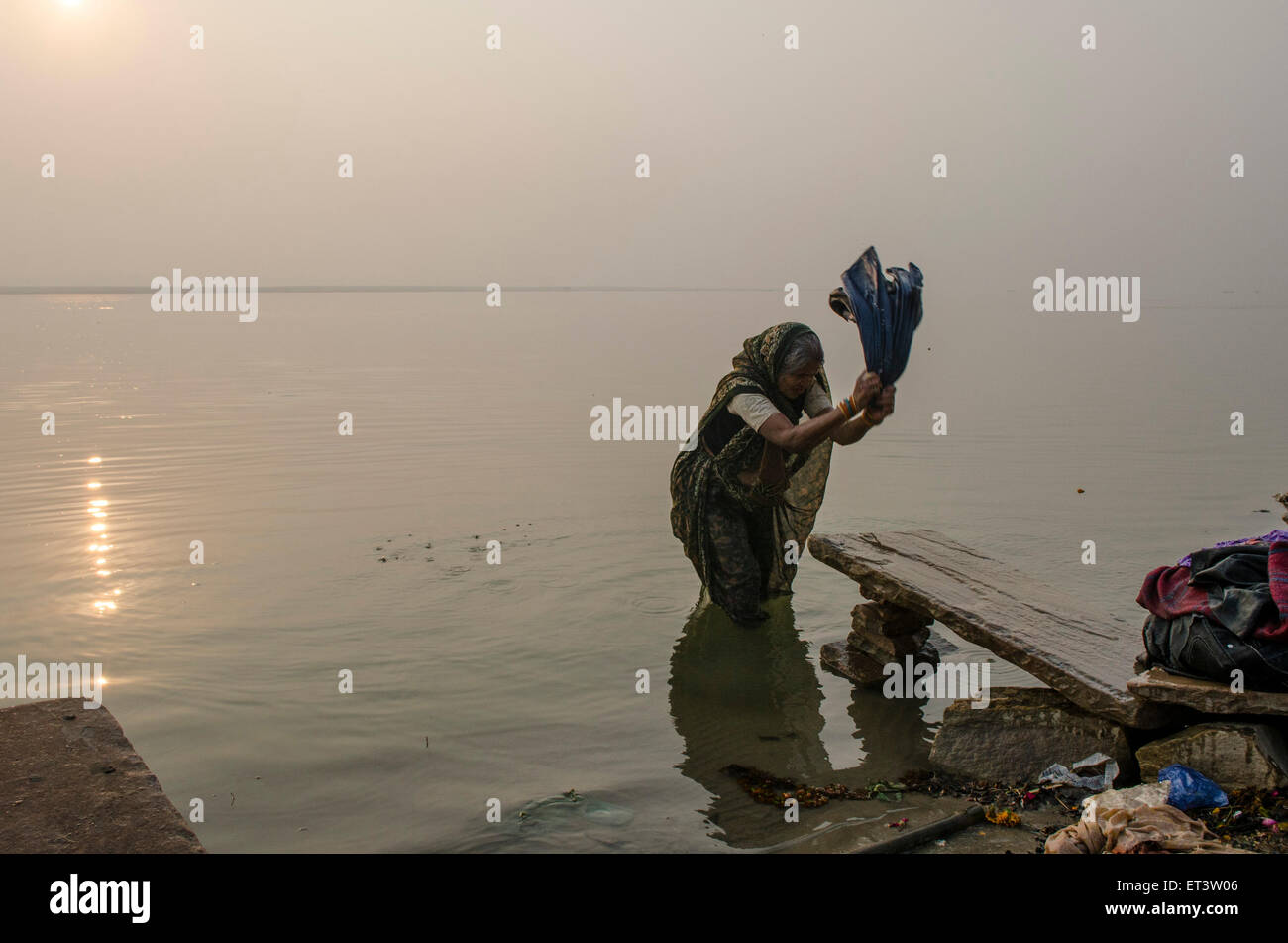 Una donna lava i suoi vestiti sulle rive del Gange a Varanasi Foto Stock