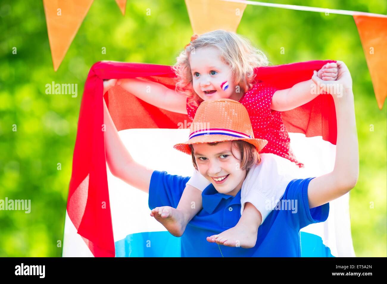 Due bambini olandesi, ragazzo adolescente e divertente bambina di celebrare la festa nazionale dei Paesi Bassi giocando in un giardino Foto Stock