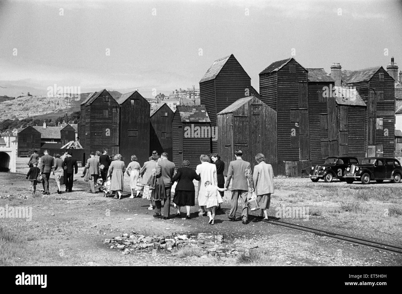 Holiday scene. in ed intorno a Hastings, East Sussex.. Passeggiata turistica sul lungomare in passato i capannoni di legno che tiene le reti da pesca dei pescatori locali. Giugno 1952. Foto Stock