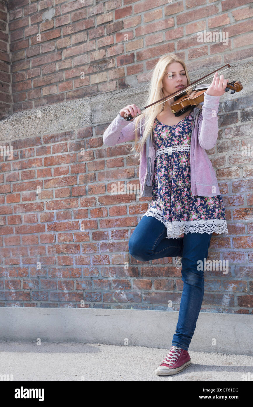 Caucasian ragazza adolescente suona il violino di fronte a un muro di mattoni, Monaco di Baviera, Germania Foto Stock
