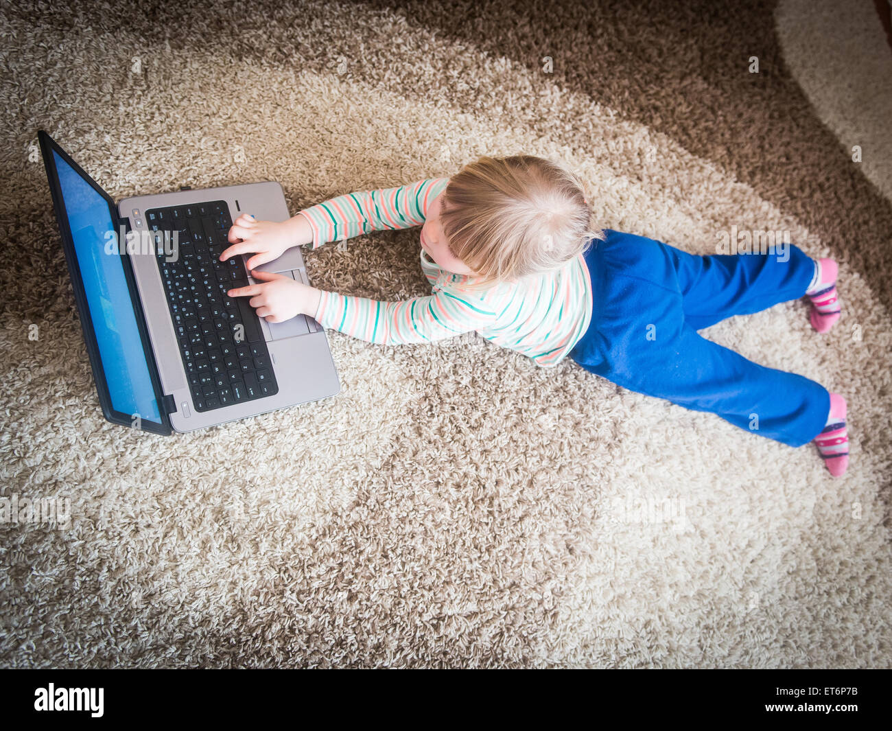 Bambina sdraiato sul pavimento e giocare su un notebook Foto Stock