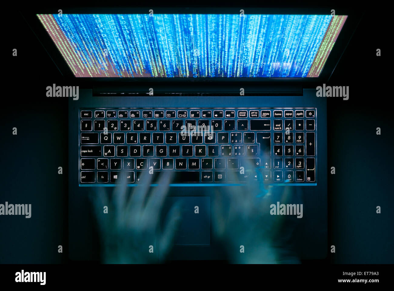 Le mani sono digitando su un computer portatile al buio con tastiera illuminata e mistico codice del programma sullo schermo Foto Stock