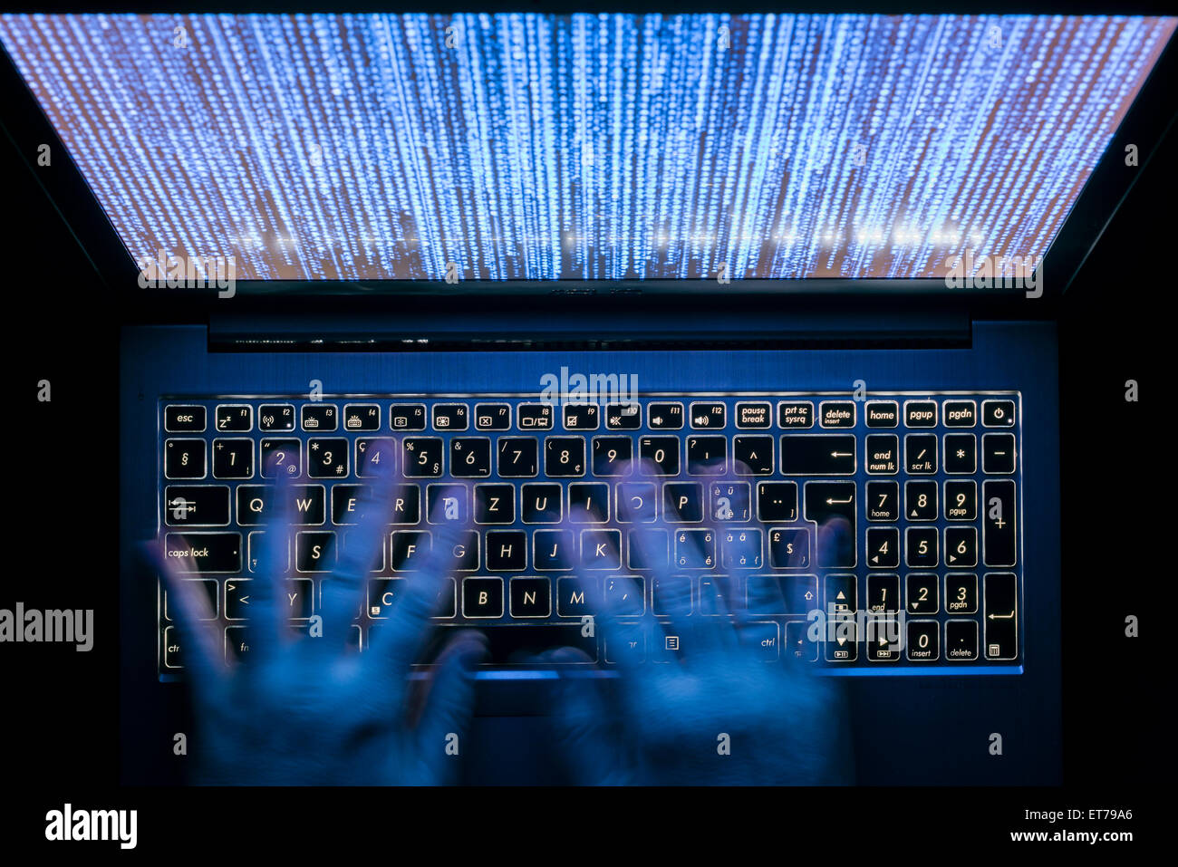 Le mani sono digitando su un computer portatile al buio con tastiera illuminata e mistico codice del programma sullo schermo Foto Stock