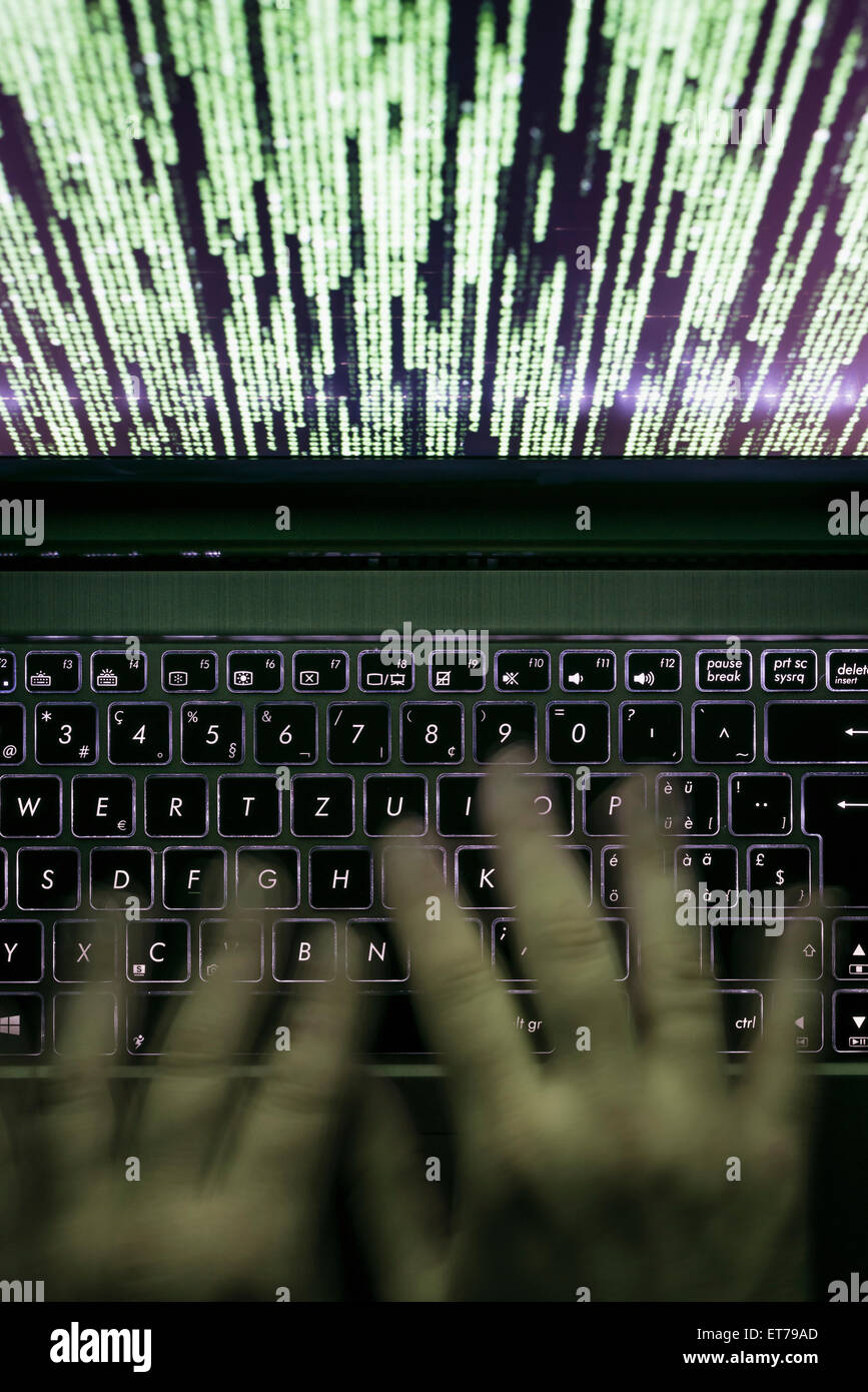 Le mani sono digitando su un computer portatile al buio con tastiera illuminata e mistico codice del programma sullo schermo Foto Stock