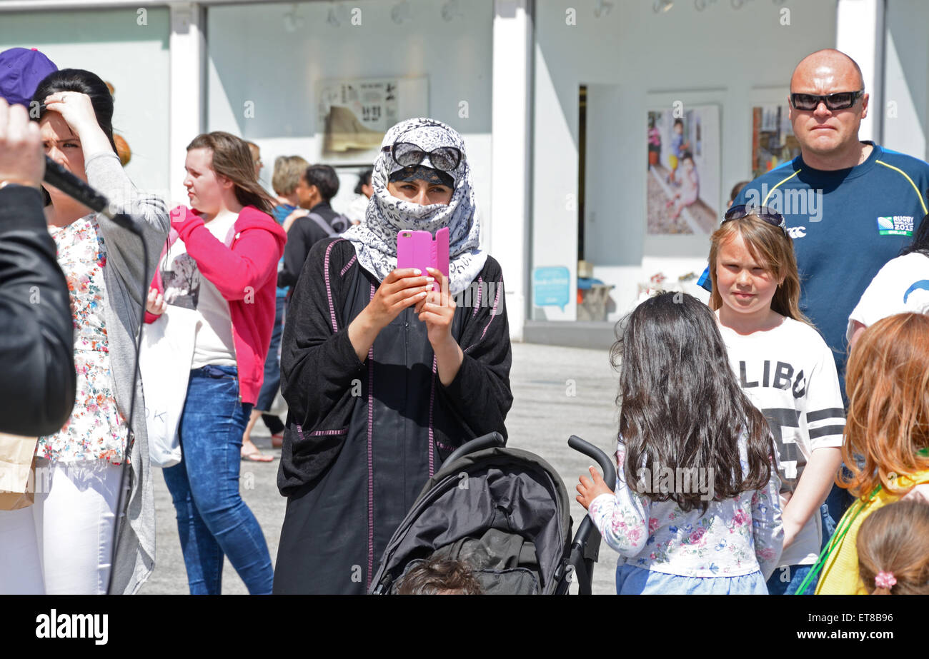 Donna musulmana in Niqab in una folla. Scattare fotografie sul telefono cellulare. Nottingham, Inghilterra. Foto Stock