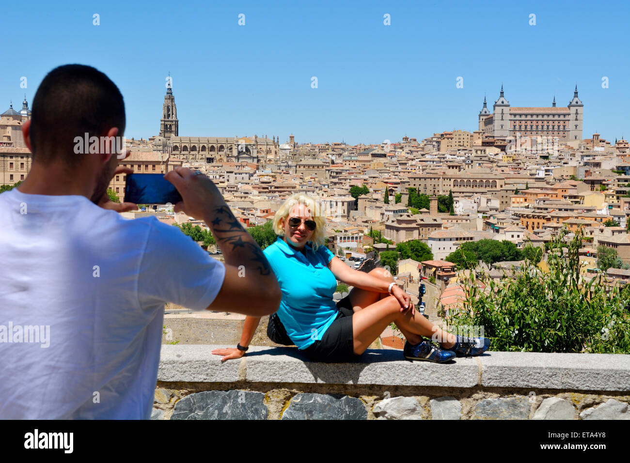 Tourist con la fotocamera del telefono di fotografare donna seduta sulla parete affacciata Toledo, Spagna Foto Stock