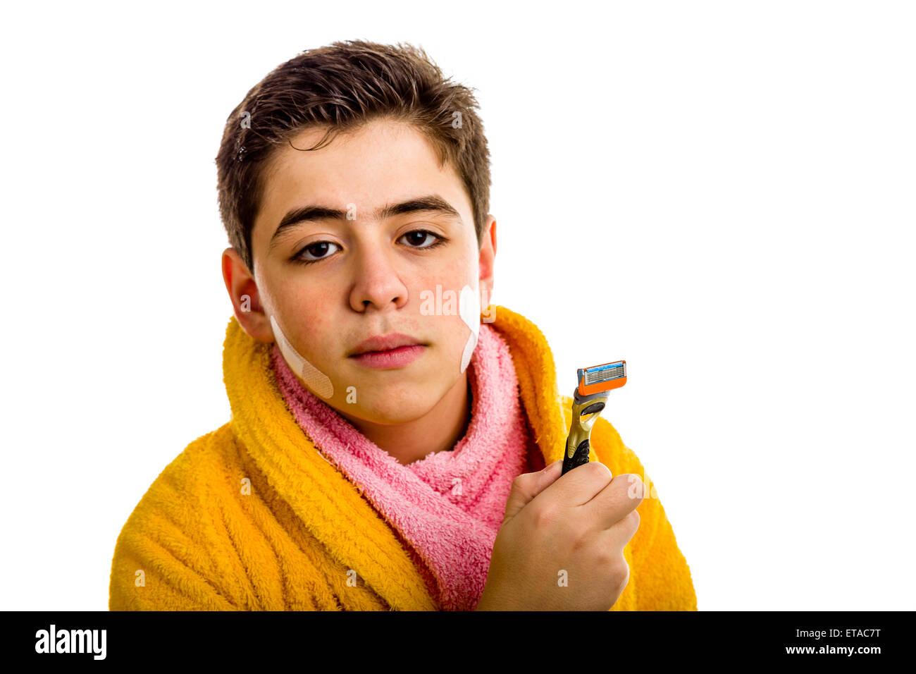 Un ragazzo ispanico indossa un accappatoio giallo con un asciugamano rosa intorno al suo collo: ha alcune patch sul suo viso e trattiene il rasoio ha utilizzato per la rasatura Foto Stock