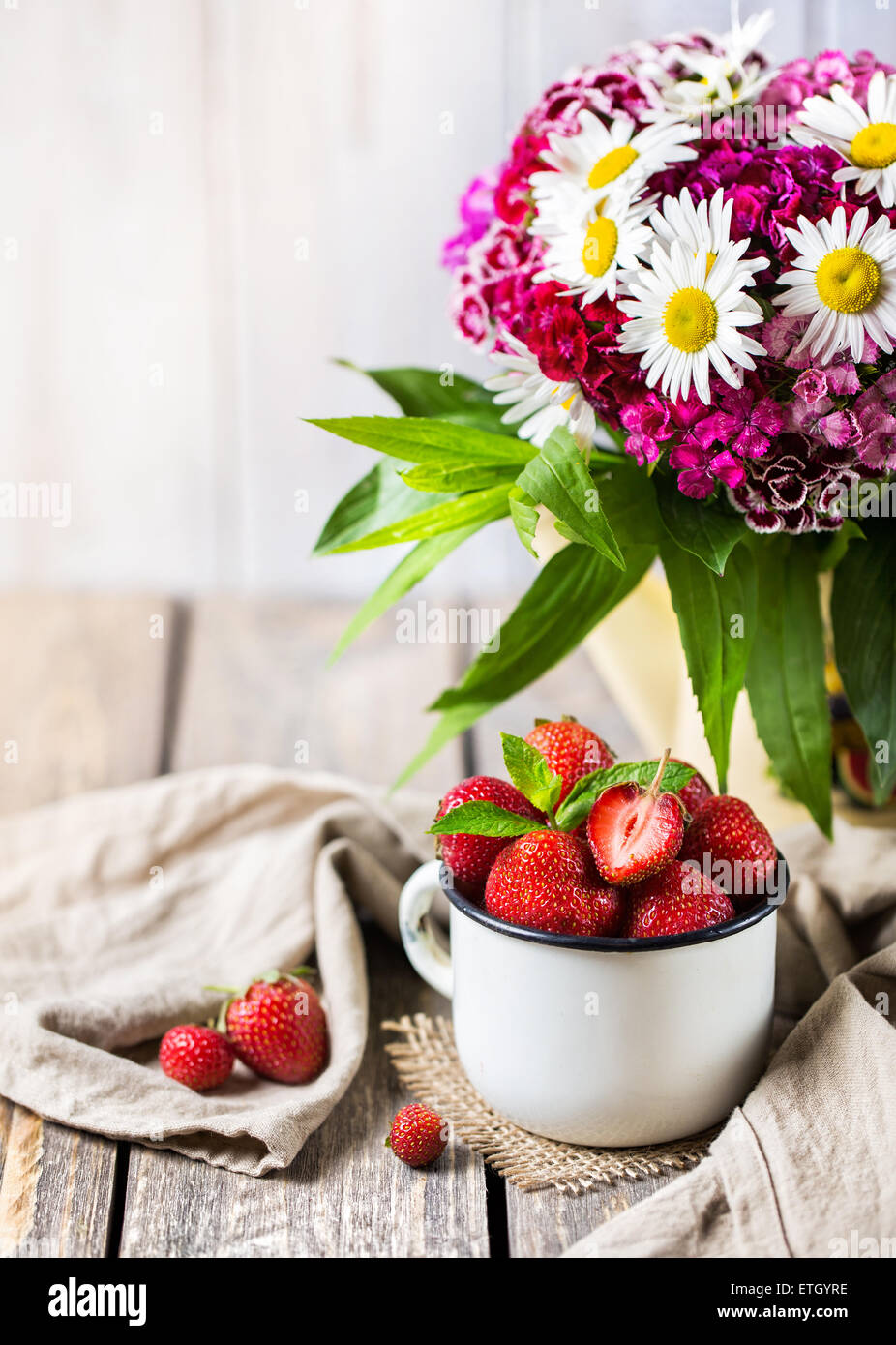 Fragola nel bicchiere vicino a bouquet di fiori sul tavolo di legno Foto Stock