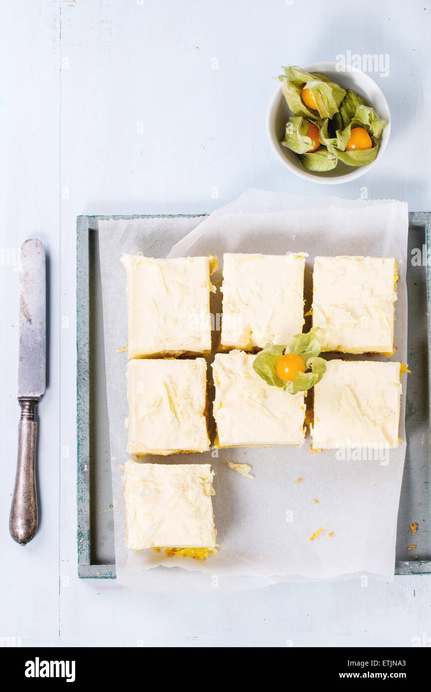 In casa fette di torta con mousse cremosa e frutti tropicali di mango e physalis servita nel vassoio in legno su fondo azzurro. Foto Stock