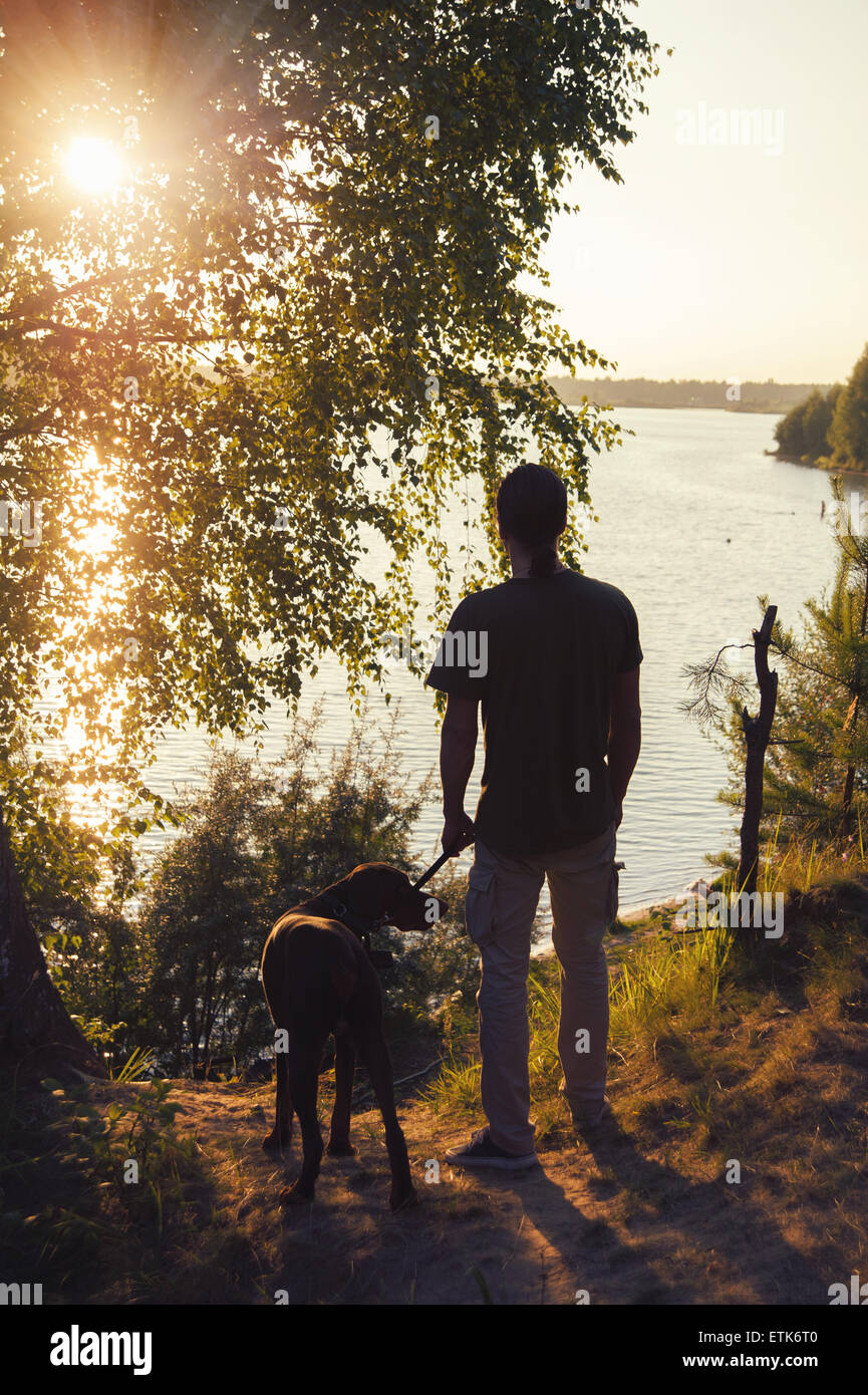 Uomo con un cane a camminare al tramonto sul lago Foto Stock