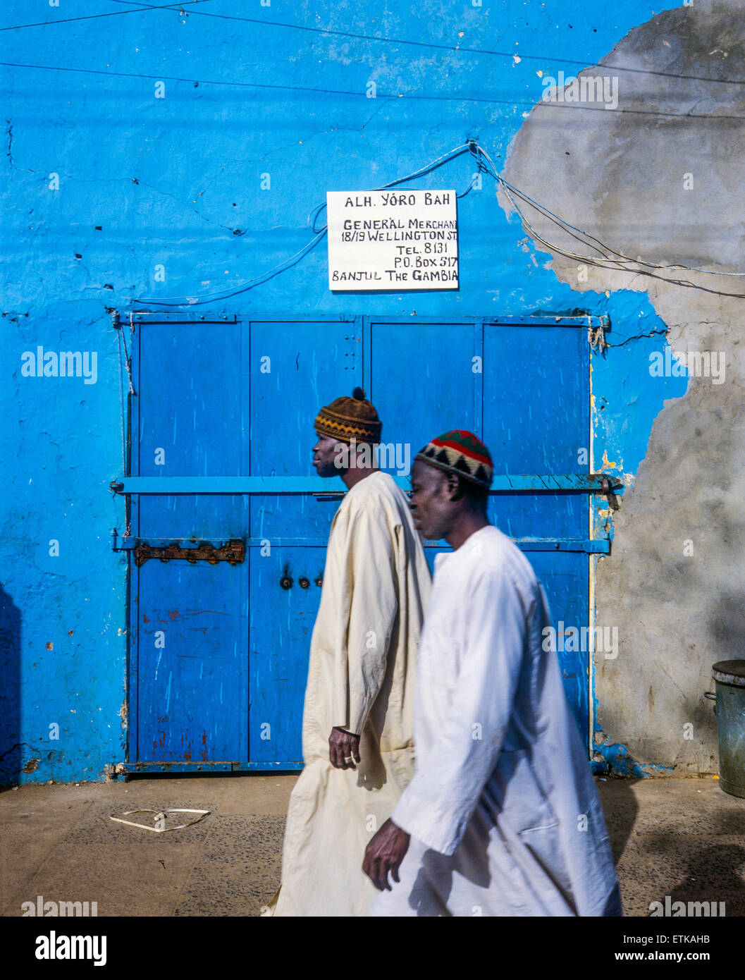 Due uomini gambiana con abiti bianchi di fronte blu porta e parete, Banjul (Gambia, Africa occidentale Foto Stock