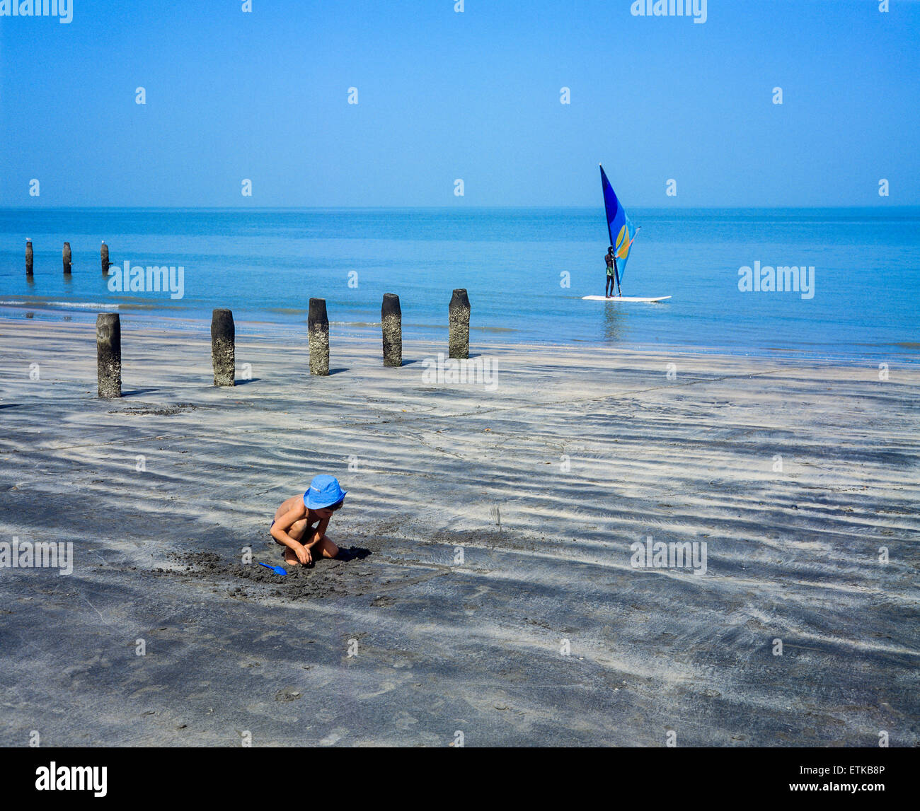 Caucasian piccolo ragazzo giocando sulla spiaggia e uomo gambiana windsurf, Gambia, Africa occidentale Foto Stock