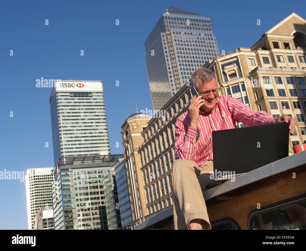 Uomo maturo che lavorano al di fuori sulla sua barca parlando su smartphone iPhone guardando al suo computer portatile Canary Wharf dietro gli uffici di Londra E14 Foto Stock
