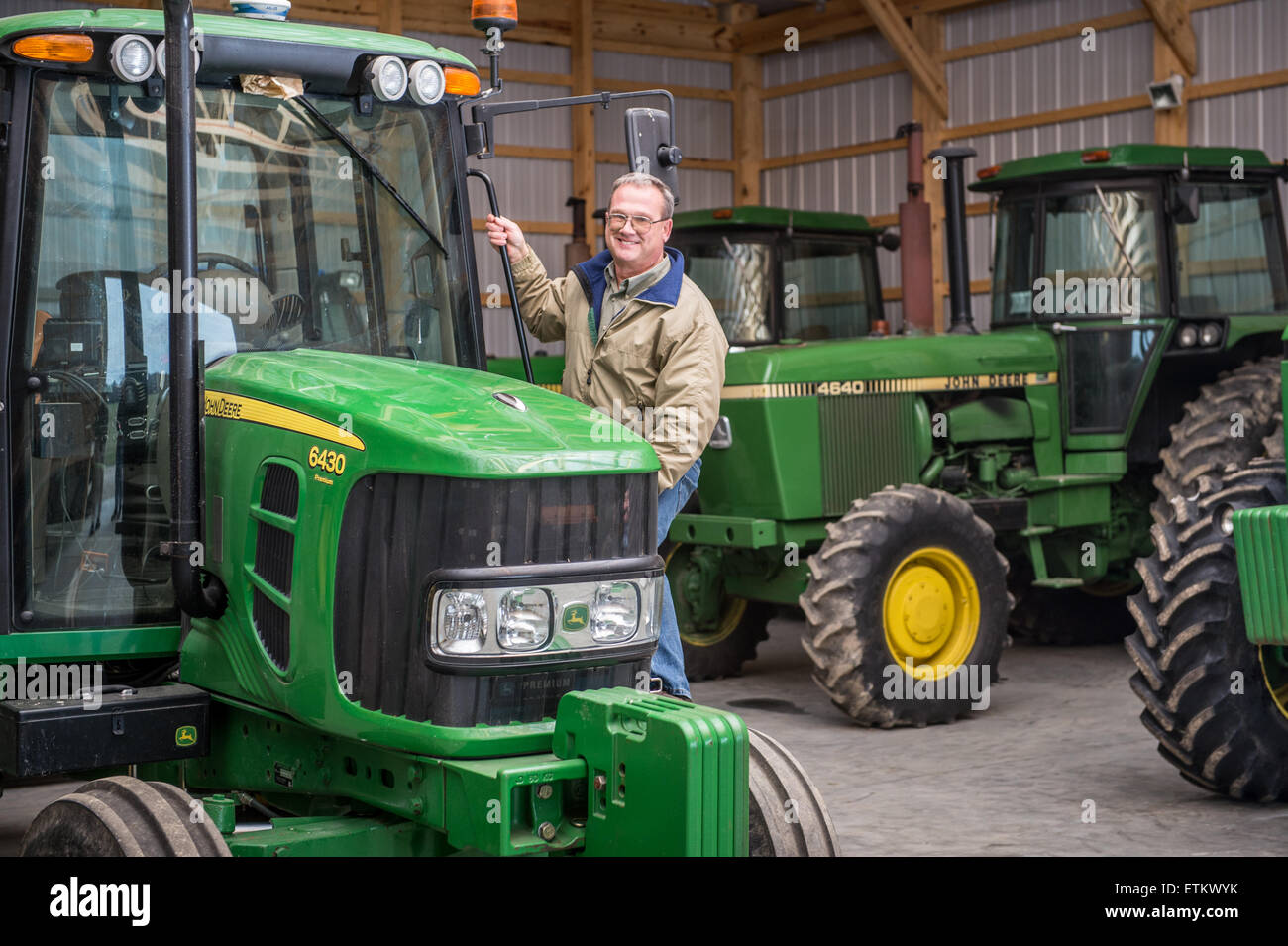 Agricoltore in piedi accanto al trattore nel capannone per il rimessaggio a Cordova, Maryland, Stati Uniti d'America Foto Stock