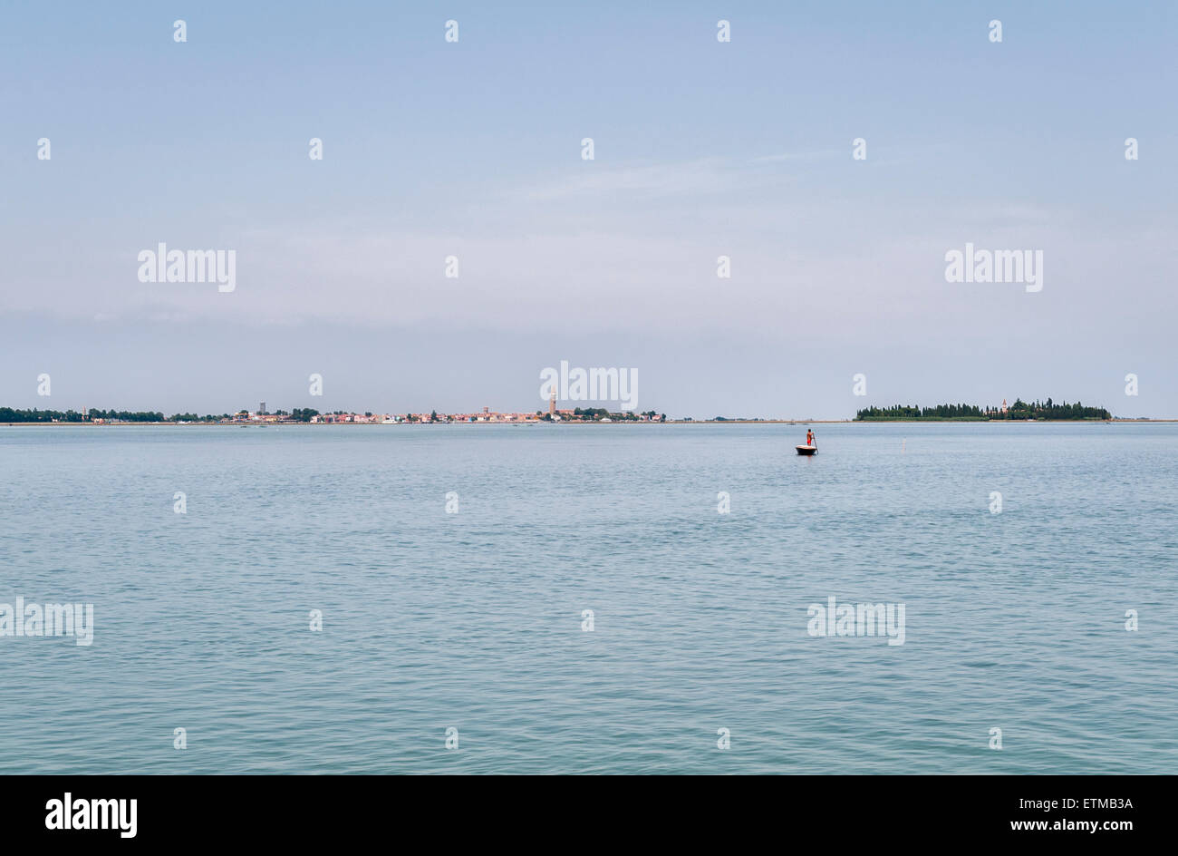 Venezia, Italia. Una vista in lontananza la città attraverso la laguna, con un uomo solitario la polarizzazione la sua barca in tutta l'acqua poco profonda Foto Stock