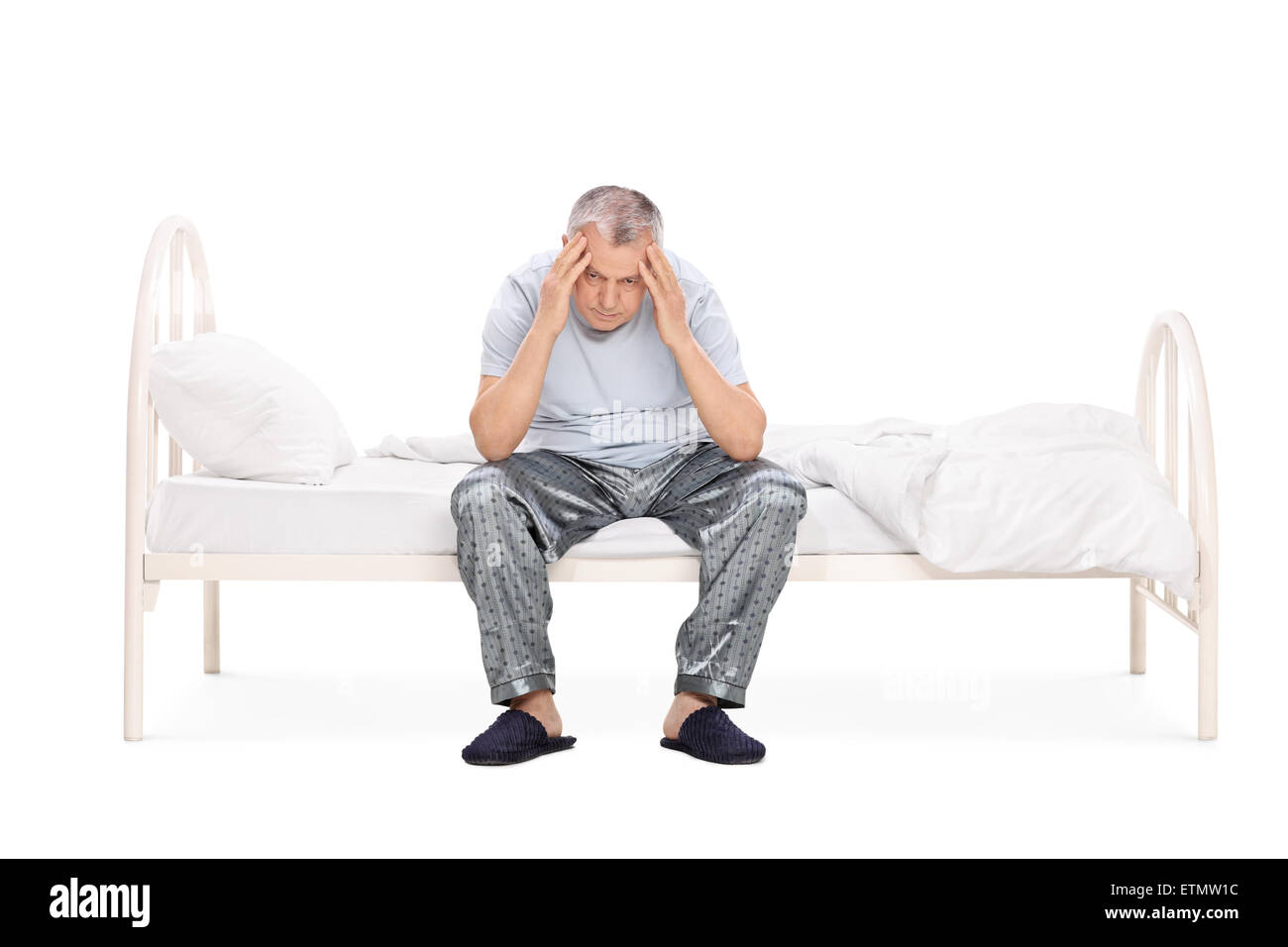 Studio shot di un frustrato senior seduto su un letto nel suo pigiama e guardando verso il basso isolati su sfondo bianco Foto Stock