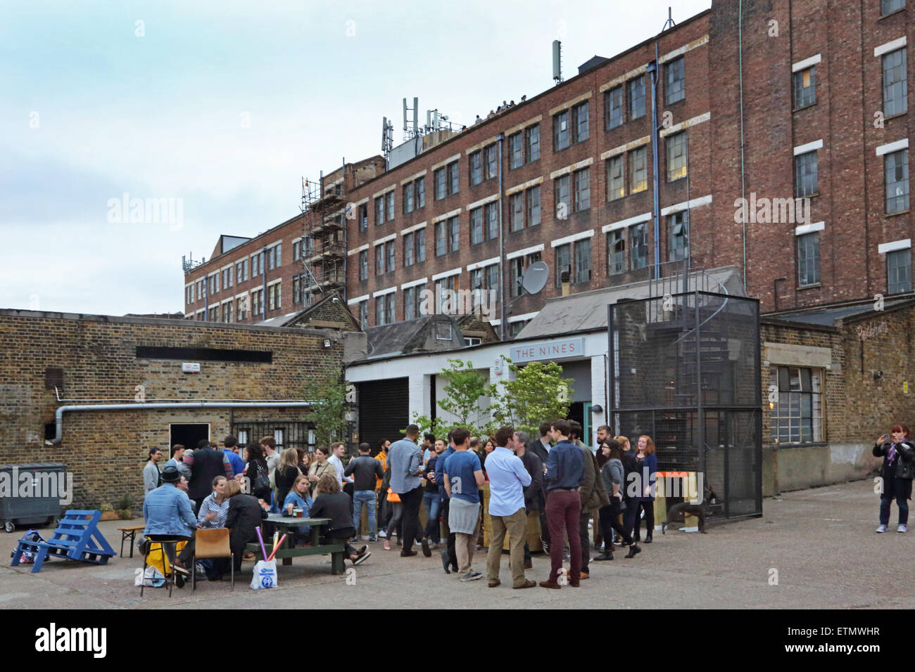 I clienti di mangiare e bere alla Nines, un pop-up bar in Peckham dietro il famoso edificio Bussey - visto in background Foto Stock