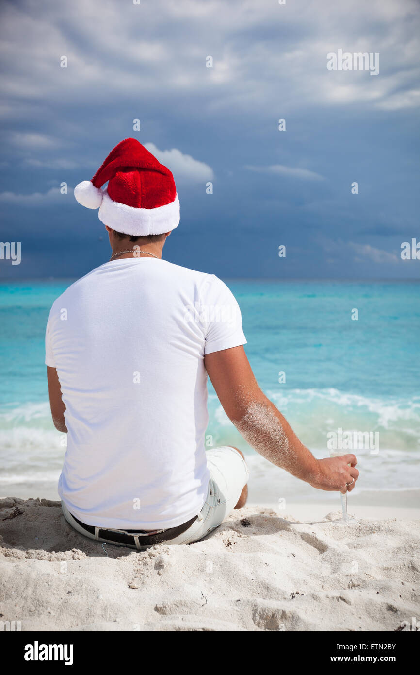 Unico Uomo in Santa Helper hat festeggiano il Natale sulla spiaggia con un bicchiere di champagne e guardando al bellissimo mare. Foto Stock