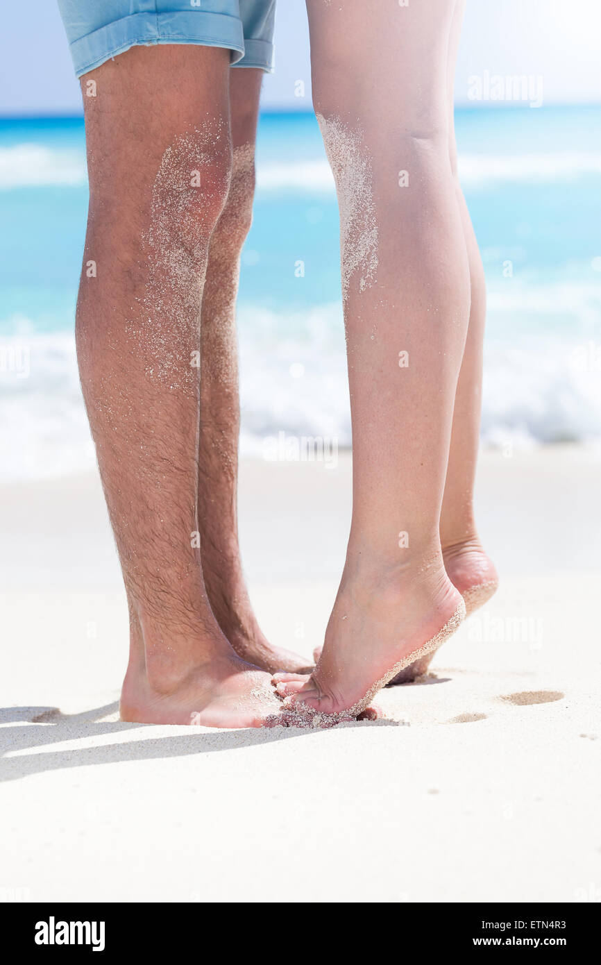 Donna gambe a piedi nudi in piedi punta di piedi closeup al piede maschile e baciare sulla spiaggia sabbiosa con mare turchese sfondo, senza volto. Foto Stock