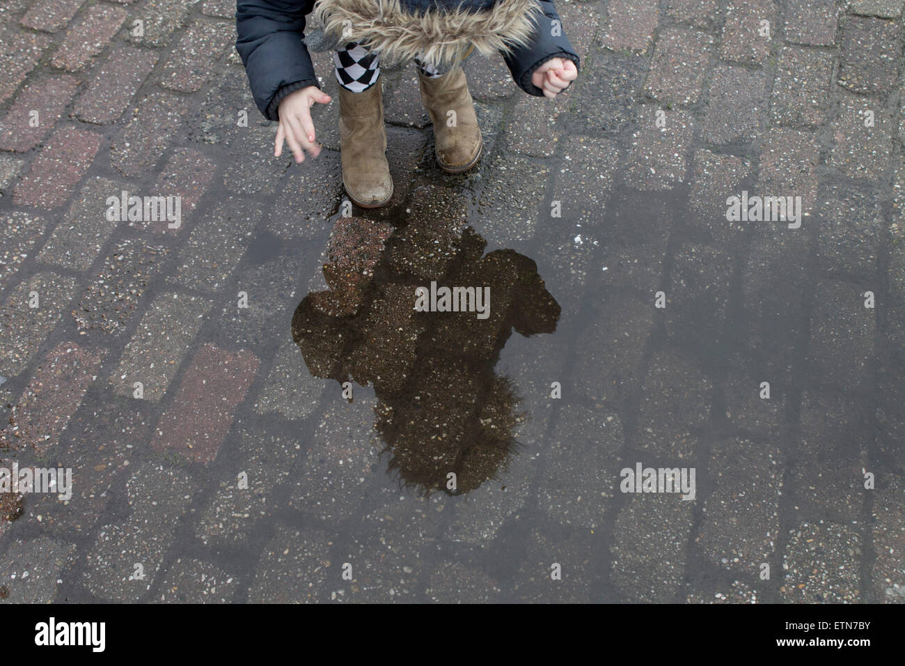 Ragazza guardando il suo riflesso in una pozza d'acqua in strada Foto Stock